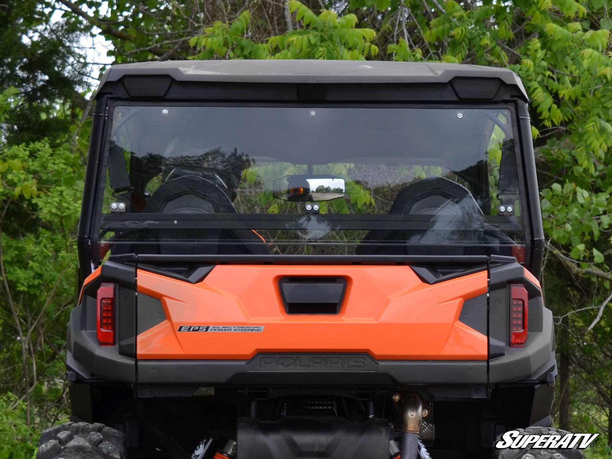 Rear view of a Polaris General XP 1000 with the SuperATV Rear Windshield, black roof, and two headrests. The vehicle is set among lush green trees. The SuperATV logo is visible in the bottom right corner.