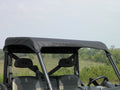 A Polaris General Soft Top covers the roof of a two-seat off-road utility vehicle parked outdoors near grassy terrain and trees under a partly cloudy sky.