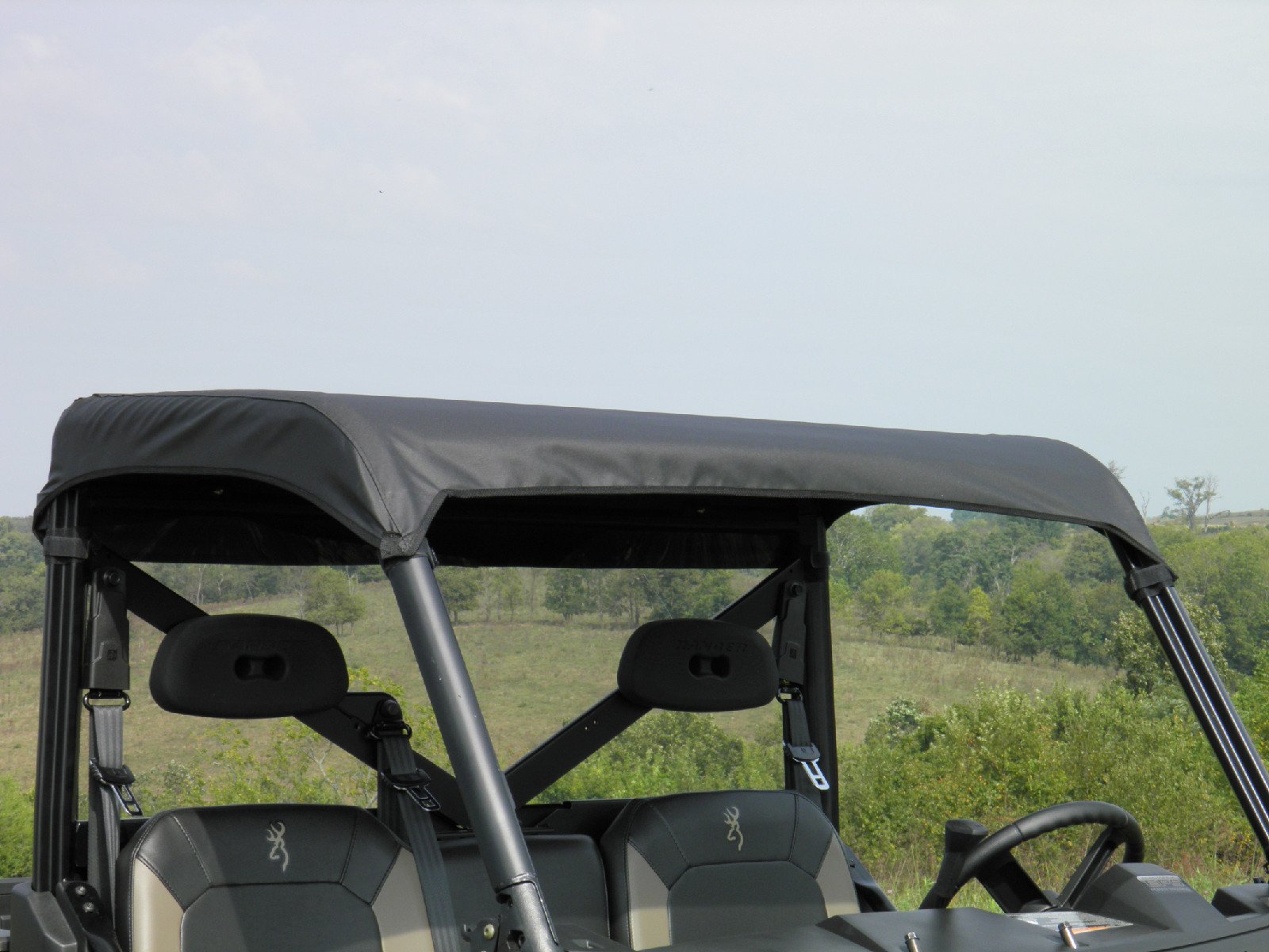 A Polaris General Soft Top covers the roof of a two-seat off-road utility vehicle parked outdoors near grassy terrain and trees under a partly cloudy sky.