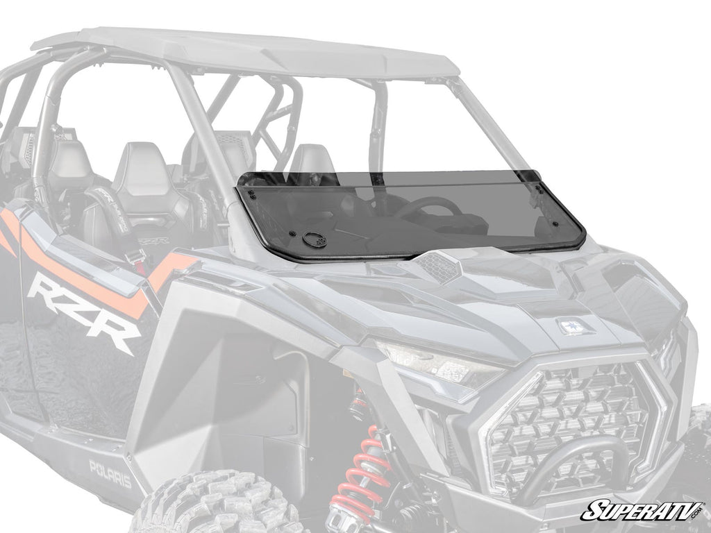 A Polaris RZR Pro S Half Windshield, tinted and mounted with visible hardware, is installed on a black and gray Polaris RZR. The half windshield covers the lower front, with the rest of the side-by-side vehicle blurred in the background.