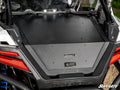 A close-up of the Polaris RZR Pro S Trunk Bed Enclosure by SuperATV shows a sturdy black metal lid with multiple bolts, the SuperATV logo, flanked by red tail lights and rugged vehicle components.