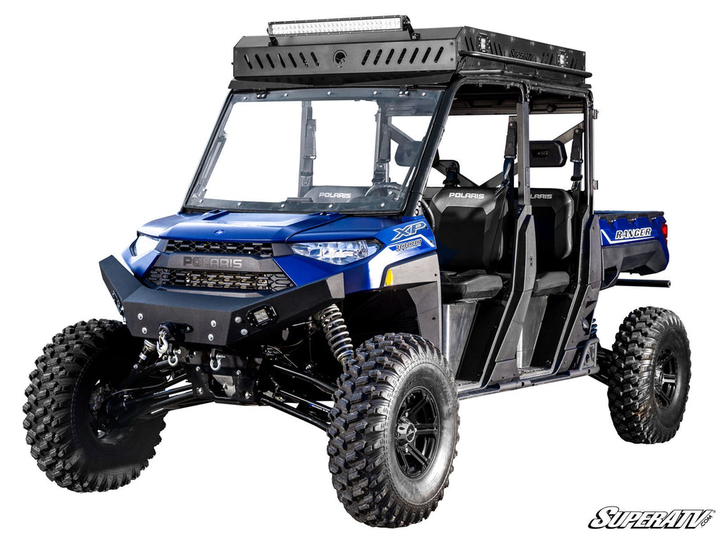 A blue Polaris Ranger XP 1000 Long Travel Kit off-road vehicle with four seats, rugged tires, roof rack, and LED light bar. Features front windshield, side doors for rough terrain, and branding stickers on the sides.