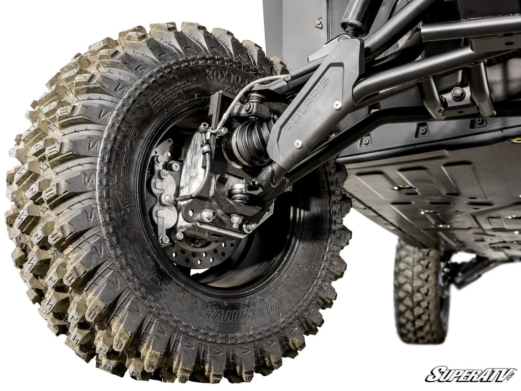 Close-up of a Polaris Ranger XD 1500 4 Portal Gear Lift shows a large, dirty off-road tire with aggressive tread, plus visible suspension parts like the control arm, shock absorber, and brake disc. SuperATV logo appears in the corner.