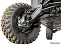 Close-up of a Polaris Ranger XD 1500 4 Portal Gear Lift shows a large, dirty off-road tire with aggressive tread, plus visible suspension parts like the control arm, shock absorber, and brake disc. SuperATV logo appears in the corner.