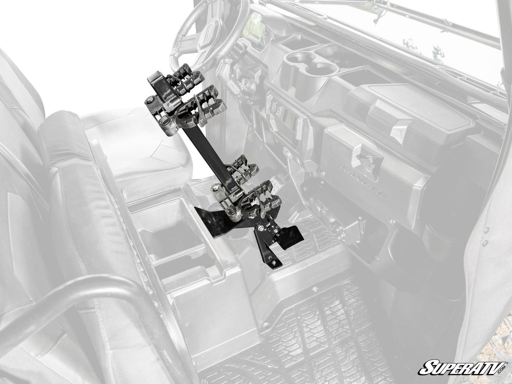 A Polaris Ranger XP 1000 Floor-Mounted Gun Holder is installed between the seats of a utility vehicle, securely holding two rifles upright. The grayscaled interior contrasts with the full-color gun holder, highlighting its design and SuperATV branding.