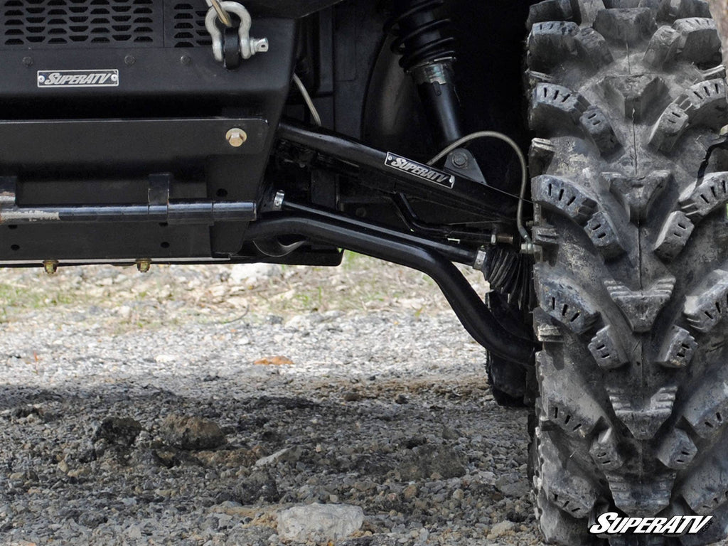 Close-up of a Polaris Ranger Full-Size 500 with High Clearance 1 Forward Offset A-Arms by SuperATV. Black SuperATV-labeled suspension arms, rugged tire, and shock absorber are visible on rocky terrain. The SuperATV logo is at the lower right.