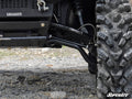 Close-up of a Polaris Ranger Full-Size 500 with High Clearance 1 Forward Offset A-Arms by SuperATV. Black SuperATV-labeled suspension arms, rugged tire, and shock absorber are visible on rocky terrain. The SuperATV logo is at the lower right.