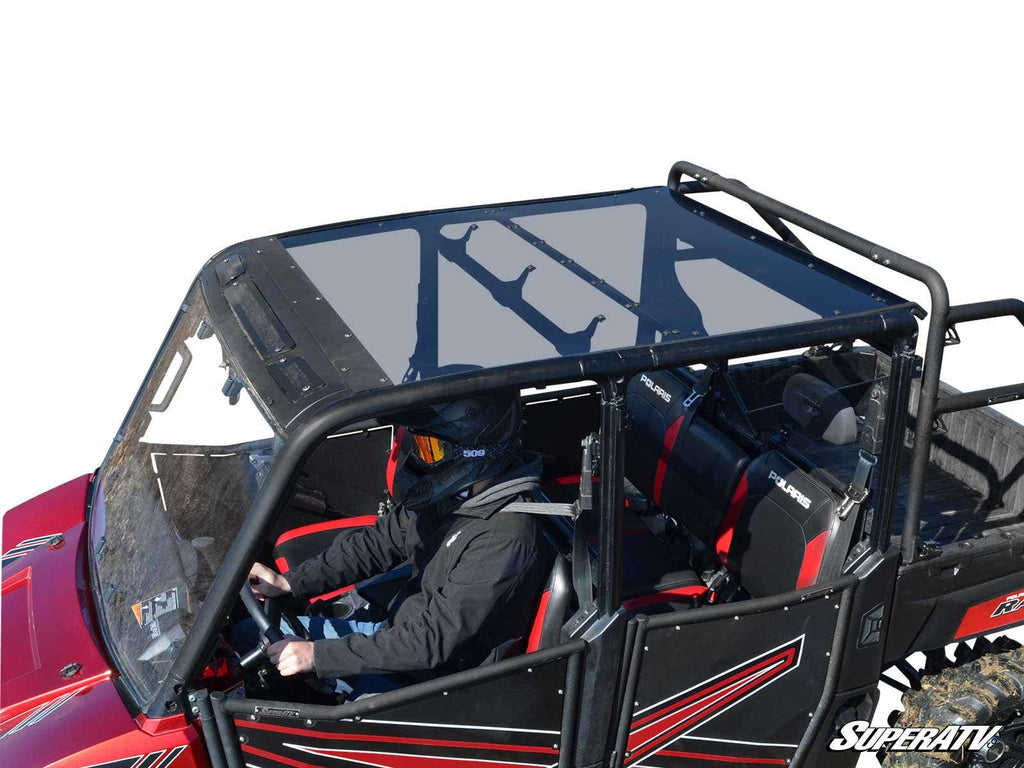 A person in a helmet and black jacket drives a red Polaris Ranger 1000 Diesel Crew with a tinted hard roof, roll cage, two visible seats with safety harnesses. The white background isolates the vehicle and driver. “SUPERATV” logo appears bottom right.
