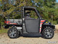 A person in a helmet sits inside a black and red Polaris Ranger 1000 Diesel equipped with Heavy-Duty Rock Slider Nerf Bars, parked on gravel outdoors with green trees in the background. SuperATV appears on the image.