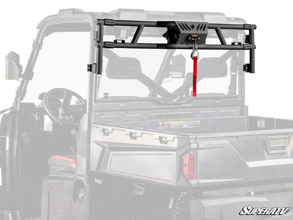 A Polaris Ranger XP 570 Game Loader Rack—finished in black—mounts on the UTV bed, holding a winch with a red strap. The vehicle is grayscale while the rack and winch appear in full color. SuperATV branding is visible in the corner.