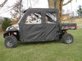 A Polaris Ranger Crew with the Soft Door Kit for all full and mid-size models is parked on grass near trees, featuring fabric door enclosures, rugged tires, a small cargo bed labeled Ranger, and a building in the background.