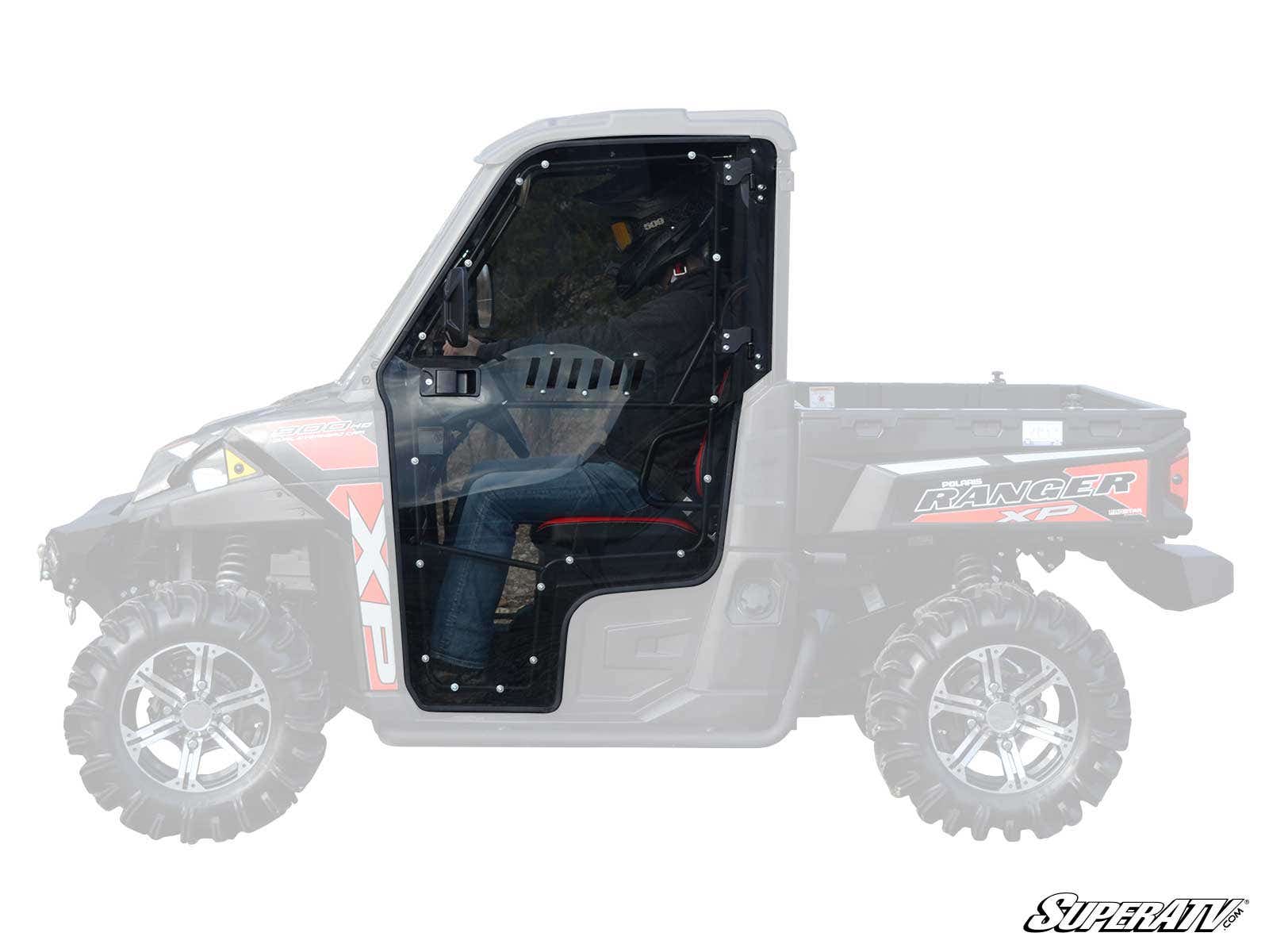 A side view shows Polaris Ranger Cab Enclosure Doors with a clear, black frame installed on a UTV. The rest of the vehicle is faded, highlighting the doors. Rugged tires and Ranger XP/XP logos are visible, with a SuperATV logo at bottom right.