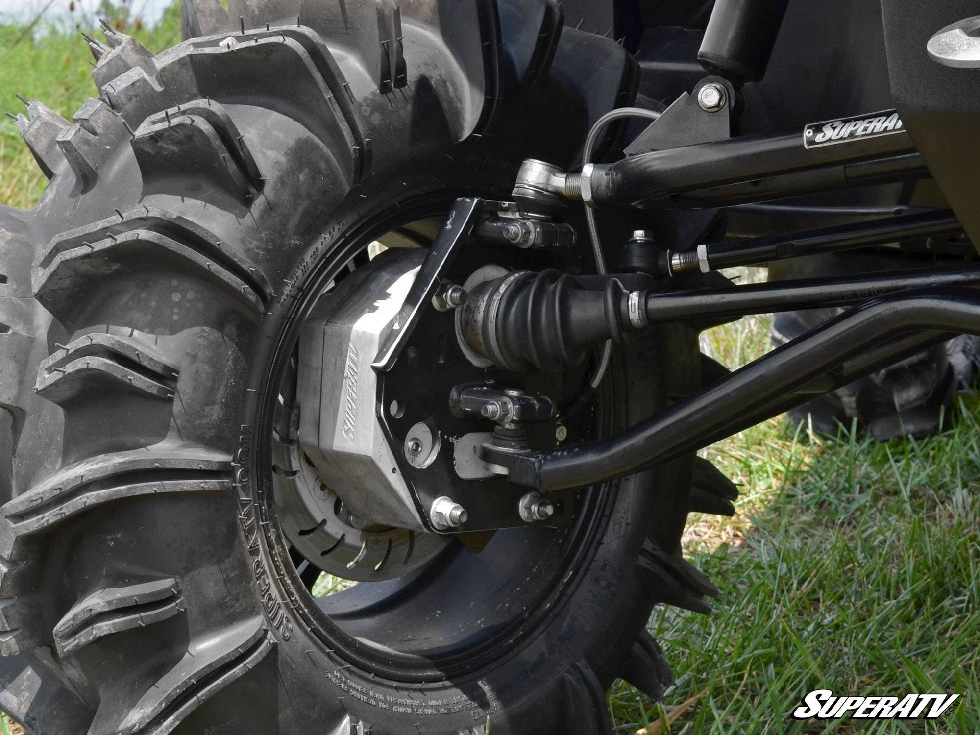 Close-up of a Polaris Ranger 1000 Diesel 4 Portal Gear Lift ATV front wheel with deep-treaded mud tire, visible disc brake, axle, suspension arms, and CV joint on grass. SuperATV logo appears in the bottom right corner.