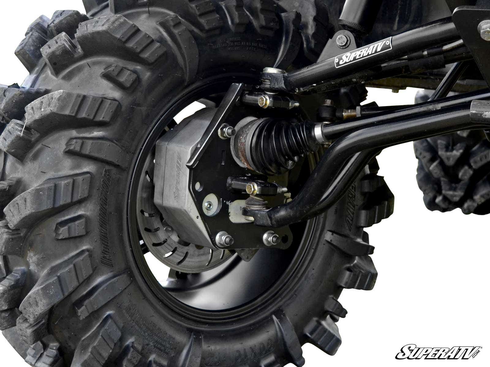 Close-up of a Polaris Ranger Full-Size 800 4 Portal Gear Lift’s large, knobby tire and suspension system, showing thick rubber treads, metal axle, springs, and drive shaft. The SuperATV logo is printed on a metal bar in the upper right corner.