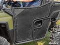 Close-up of Polaris Ranger Full-Size 570 Aluminum Doors in black metal on an olive green off-road vehicle. A person is inside, holding the steering wheel, with SuperATV branding shown on grassy ground.