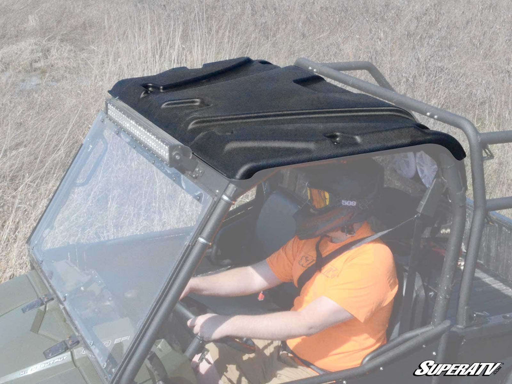 A person in an orange shirt and black helmet drives a Polaris Ranger XP 800 with a Plastic Roof and metal roll cage across dry grass, seen from above. The SuperATV logo is visible in the bottom right corner.