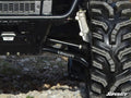 Close-up of the Polaris Ranger Midsize EV High Clearance A-Arms and rugged tire on rocky terrain. The black SuperATV suspension arms and Polaris brake caliper emphasize the vehicle’s robust build and quality components.