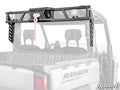 A black metal Polaris Ranger XD 1500 Game Loader Rack with a winch and pulley is mounted on a gray utility vehicle bed. The rack features angled supports, a red strap from the winch, and SUPERATV branding in the lower right corner.