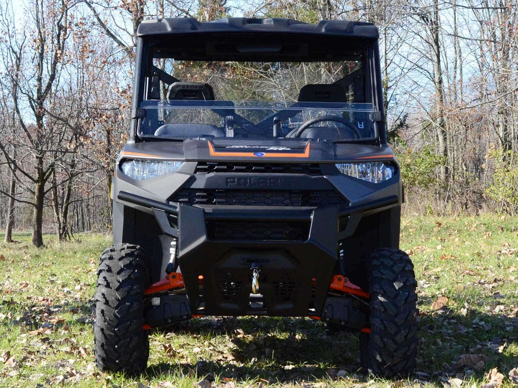 A black utility vehicle with a Polaris Ranger XP 570 Half Windshield and large rugged tires is parked on grass, with trees and dry leaves in the background, hinting at a fall setting.