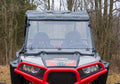 A Polaris RZR S 1000 equipped with a flip down windshield is shown front-facing in black and red, featuring two bucket seats and a detailed dashboard. The background of bare trees and brown grass suggests late autumn or early winter.