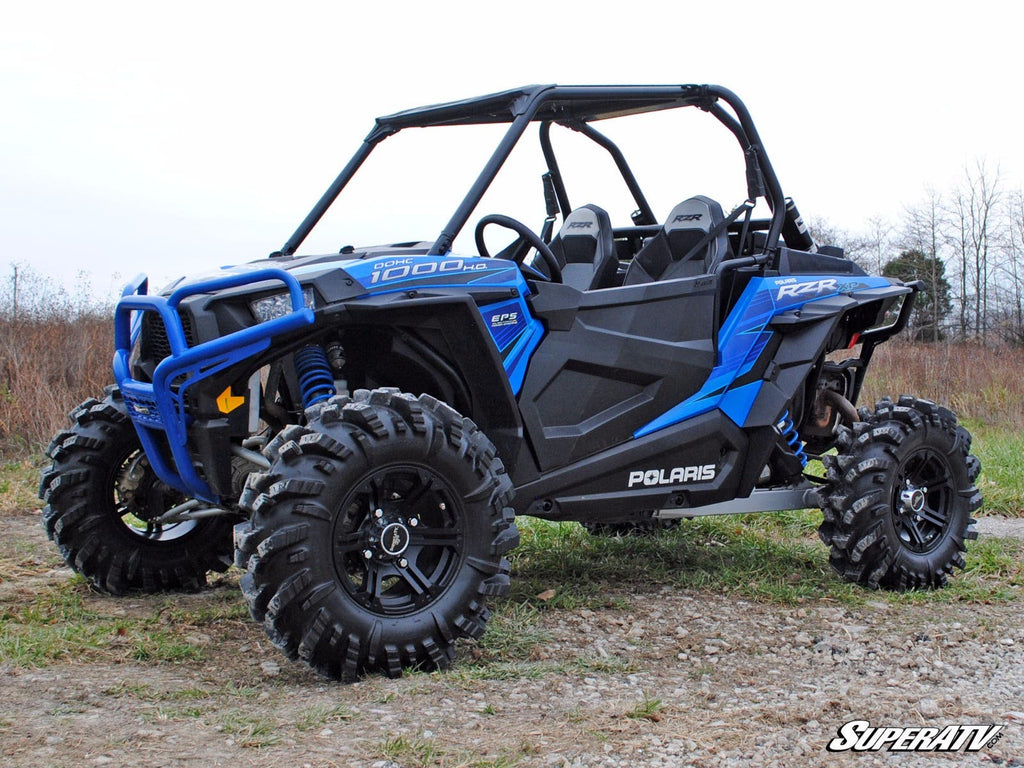A Polaris RZR XP Turbo with Plastic Doors and large rugged tires is parked on rocky terrain, featuring roll bars, bucket seats, and bold POLARIS branding. Sparse grass and an overcast sky appear in the background.