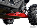 Close-up under a Polaris RZR XP 1000 shows its Rear Trailing Arms, large rugged tires, red SuperATV suspension component, coiled shock absorber, and armored skid plate—highlighting the vehicle’s robust build and all-terrain suspension system.