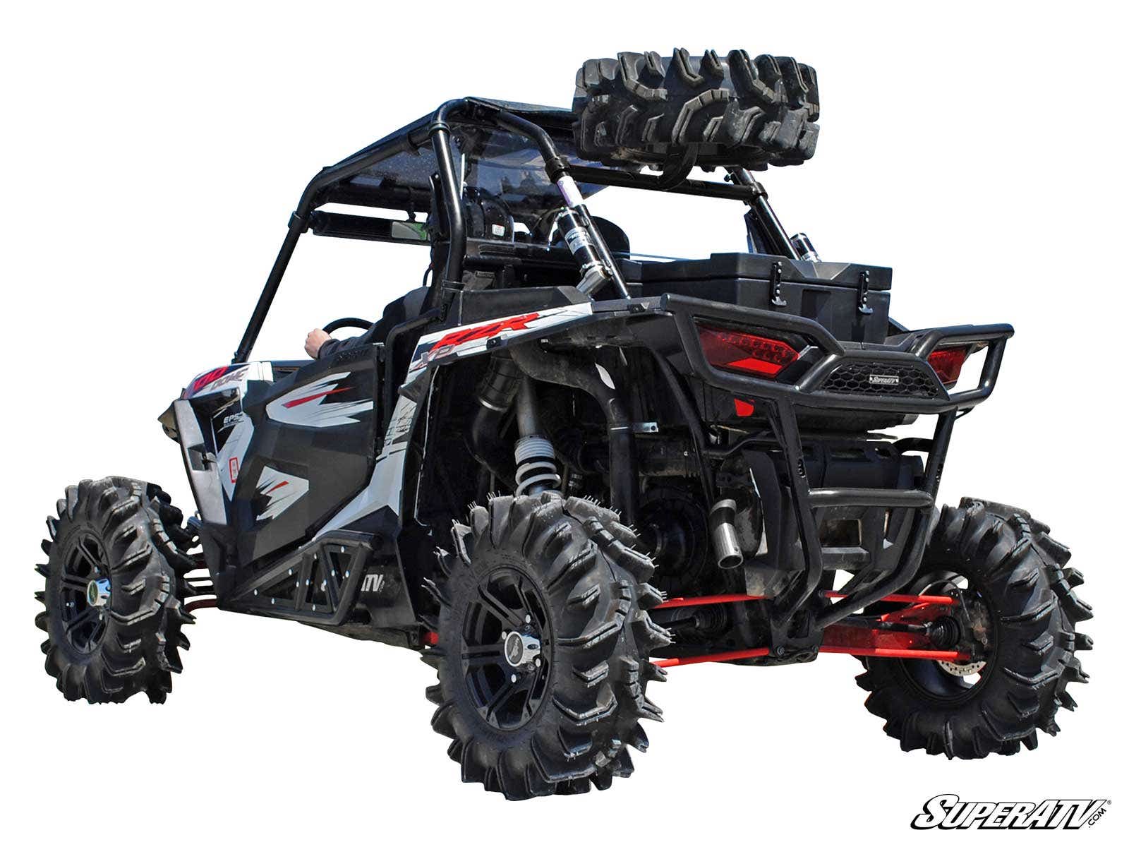 A Polaris RZR XP Turbo equipped with a black and red spare tire carrier, large rugged tires, roll cage, and extra spare tires mounted on the rear cargo rack, viewed from the back left side against a white background.