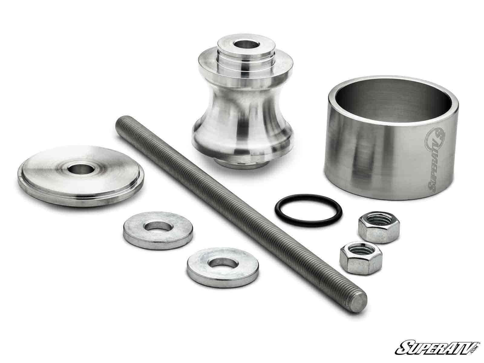 The Polaris Wheel Bearing Removal Tool set includes silver-colored metal parts—a threaded rod, two hex nuts, two washers, a spacer, a domed cap, a spool-shaped piece, a rubber O-ring, and a SuperATV-branded cylinder—displayed on a white background.