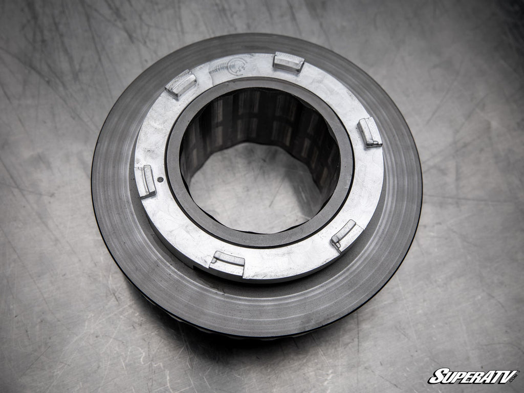 A close-up of a Polaris Ranger Billet Torsion Spring Retainer shows its round shape, grooved edges, and rectangular tabs on a scratched metallic surface. The SuperATV logo is visible in the lower right corner.