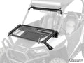 A Polaris RZR S 1000 Flip Down Glass Windshield with a black frame is mounted on an off-road vehicle. The transparent windshield is partially open, revealing its hinges and hardware, with the SuperATV logo at the bottom right.