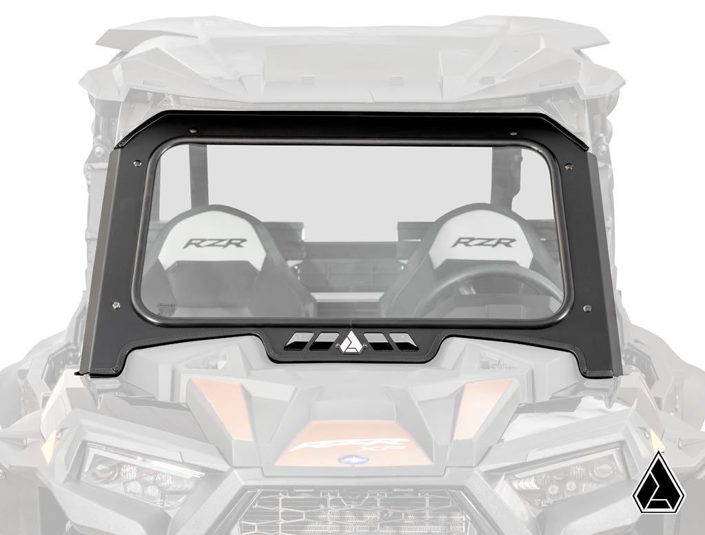 A clear, rectangular Assault Industries Polaris RZR XP Turbo Glass Windshield with a black frame is mounted on a Polaris RZR side-by-side vehicle, showing two RZR-labeled seats and the manufacturers logo in the lower right corner.