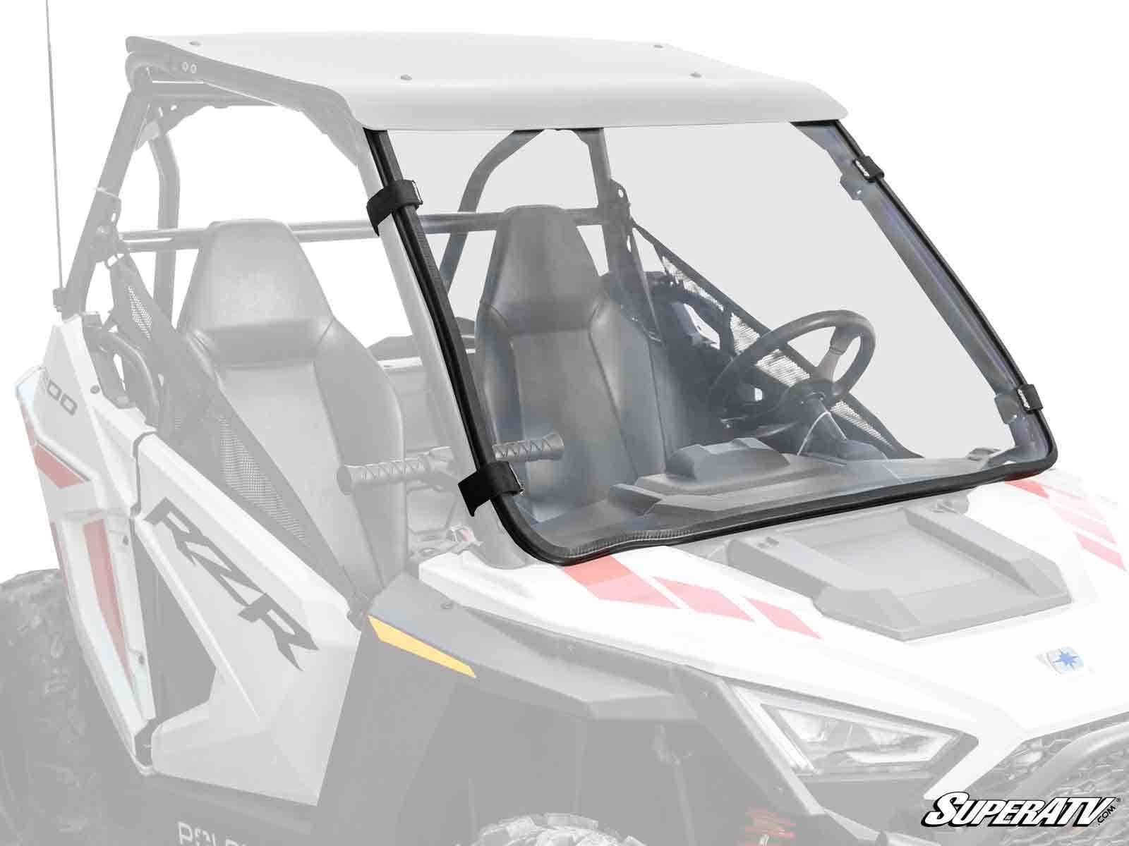 A white Polaris RZR with two bucket seats, a roof, and a visible steering wheel features the Polaris RZR 200 Full Windshield. The clear windshield covers the front and is secured on both sides with black clamps.