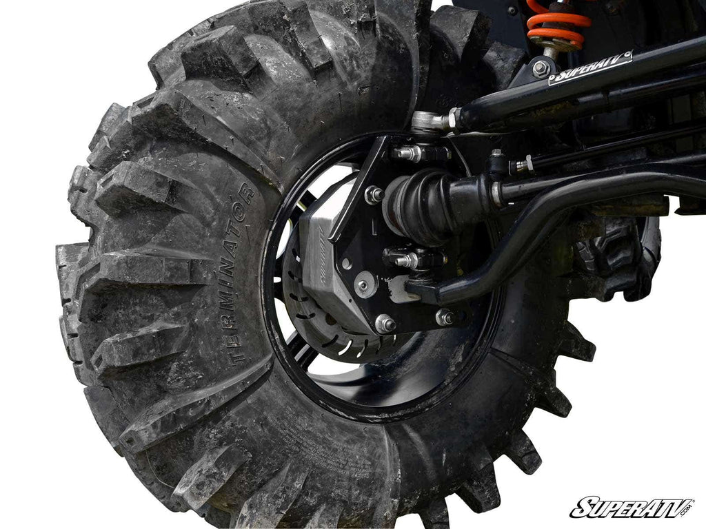 Close-up of a large, muddy off-road tire on a black rim, showing the suspension and disc brake of a Polaris RZR 570 with 4 Portal Gear Lift. The SuperATV logo is in the bottom right corner.
