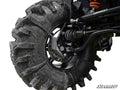 Close-up of a large, muddy off-road tire on a black rim, showing the suspension and disc brake of a Polaris RZR 570 with 4 Portal Gear Lift. The SuperATV logo is in the bottom right corner.