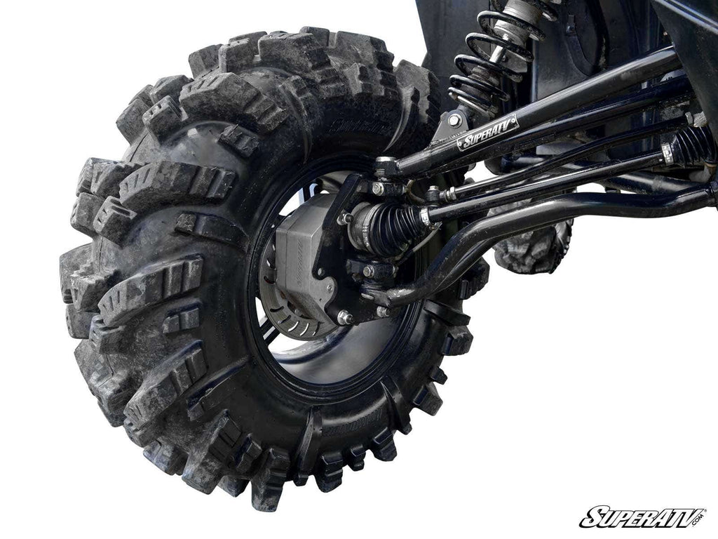 Close-up of a Polaris RZR XP 900 4 Portal Gear Lift installed, showing a rugged off-road tire with deep treads covered in mud and dirt. Branded components, visible shock absorber, and SuperATV logo featured in the bottom right corner.
