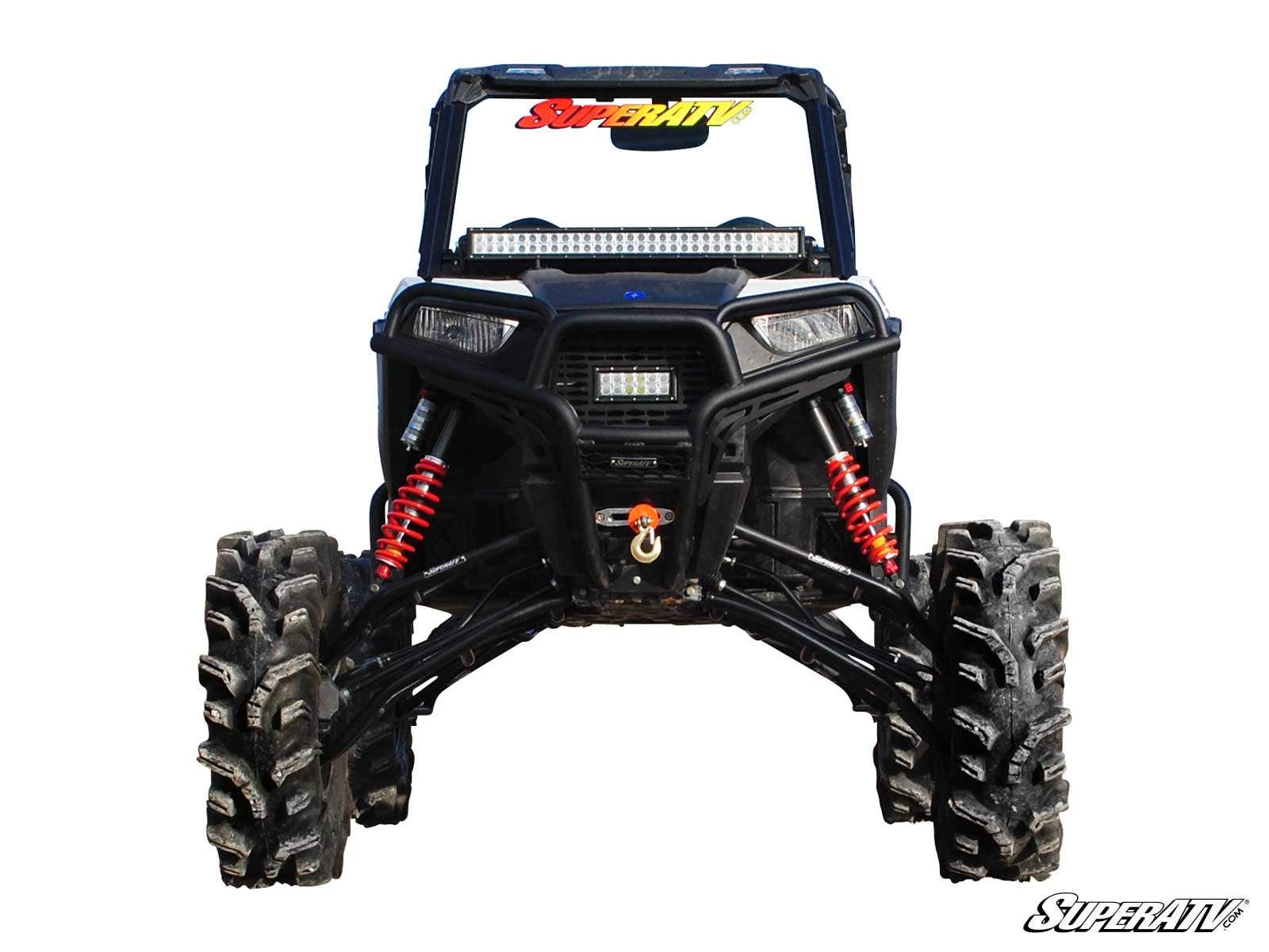 A front-facing black Polaris RZR Trail 900 with a 7-10 Lift Kit, large rugged tires, red suspension springs, LED light bars, and a winch. The windshield shows a colorful SuperATV logo; the white background features the SuperATV watermark.