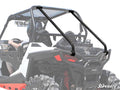 A close-up of a Polaris RZR S 1000 with rear cage support, showing diagonal bars, black seats, and a helmeted driver. The white background highlights the vehicle’s rear and the SuperATV logo in the bottom right corner.