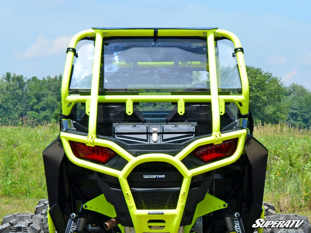 A Polaris RZR 900 with a rear windshield is shown from the back on grass with trees behind it. The off-road vehicle features red tail lights, black panels, and a SuperATV logo, highlighting its rugged, outdoor-ready style.
