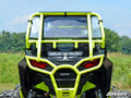 A Polaris RZR 900 with a rear windshield is shown from the back on grass with trees behind it. The off-road vehicle features red tail lights, black panels, and a SuperATV logo, highlighting its rugged, outdoor-ready style.