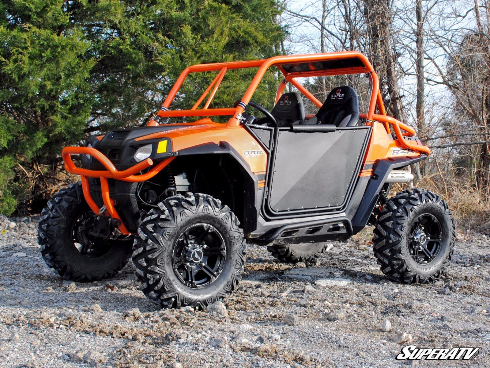 An orange off-road side-by-side with black accents, knobby tires, roll cage, doors, and two bucket seats sits on rocky terrain. It features a lifted suspension using the Polaris RZR 4 800 2-3 Lift Kit and has “SuperATV” branding visible.