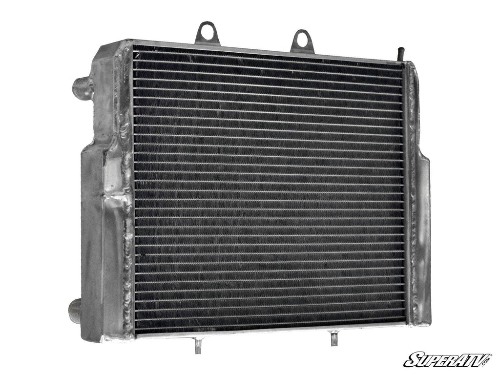 The Polaris RZR Heavy-Duty Radiator features a metal build with horizontal cooling fins, two top mounting tabs, side inlet and outlet pipes, a rugged surface, and the SuperATV logo in the lower right corner.