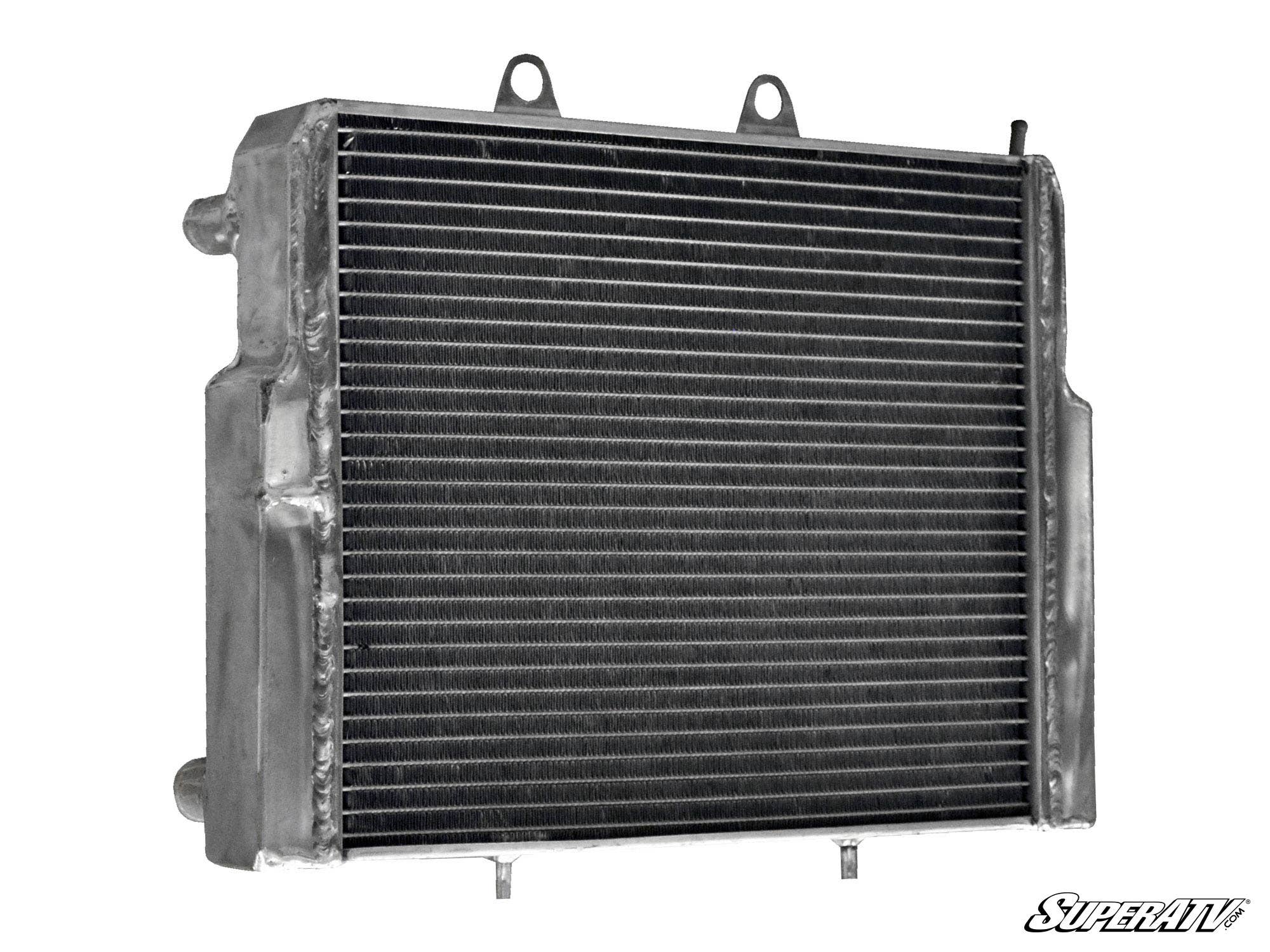 The Polaris RZR Heavy-Duty Radiator features a metal build with horizontal cooling fins, two top mounting tabs, side inlet and outlet pipes, a rugged surface, and the SuperATV logo in the lower right corner.