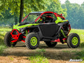 A Polaris RZR Pro R with neon green and red accents, large rugged tires, and Polaris RZR Pro R Aluminum Doors is parked on a dirt path amid trees and grass. “SuperATV” branding appears in the bottom right corner.