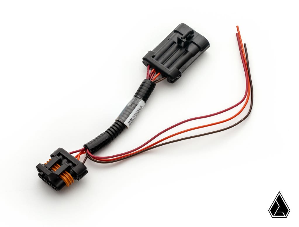 A close-up of the Assault Industries Piggyback Tail Light Harness for Polaris RZR shows black connectors, an orange gasket, and four colored wires (red, brown, black, orange) on a white background with a small black triangle logo in the lower right.
