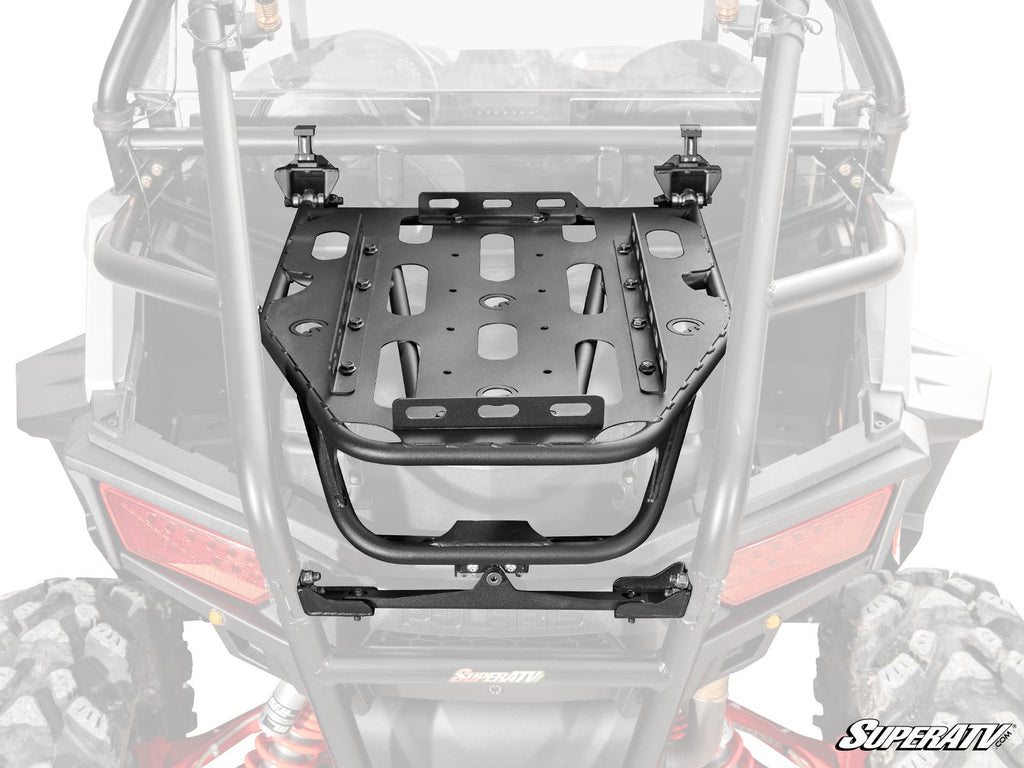 The Polaris RZR Trail 900 Cargo Rack Alpha, a black metal rack with multiple slots and cutouts for securing gear, is mounted on the rear of an off-road vehicle. It attaches with brackets and clamps; the rear roll cage and taillights are partially visible.