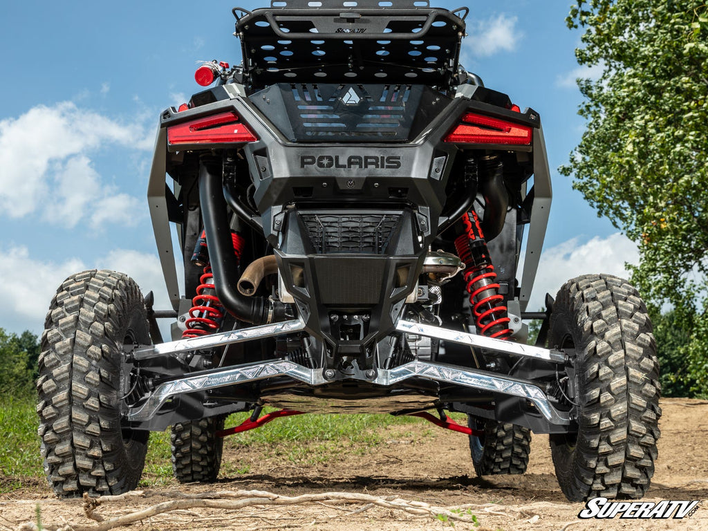 Rear view of a black Polaris off-road vehicle with Polaris RZR Turbo R Trailing Arms, large rugged tires, red shocks, and “Polaris” branding on a dirt trail. Green grass and trees under a blue sky; SuperATV logo in the corner.