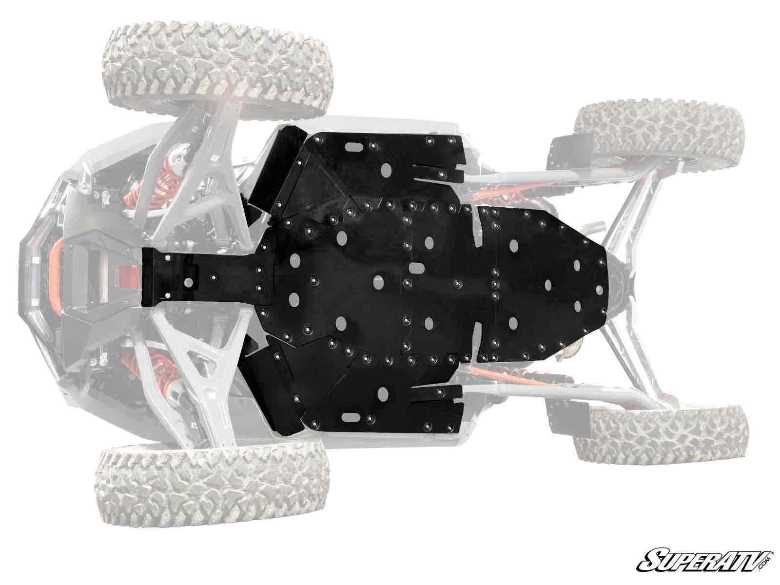 View of a Polaris RZR Turbo R Full Skid Plate in solid black installed beneath the vehicle, with large rugged tires and suspension visible. The rest of the off-road vehicle is faded. “SuperATV” logo appears at the lower right corner.
