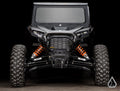 Front view of a black off-road vehicle with Assault Industries Polaris RZR XP High-Clearance 1.5 Forward Offset Boxed A-Arms, rugged tires, exposed orange suspension springs, angular body lines, bright headlights, winch, and hexagonal grille.