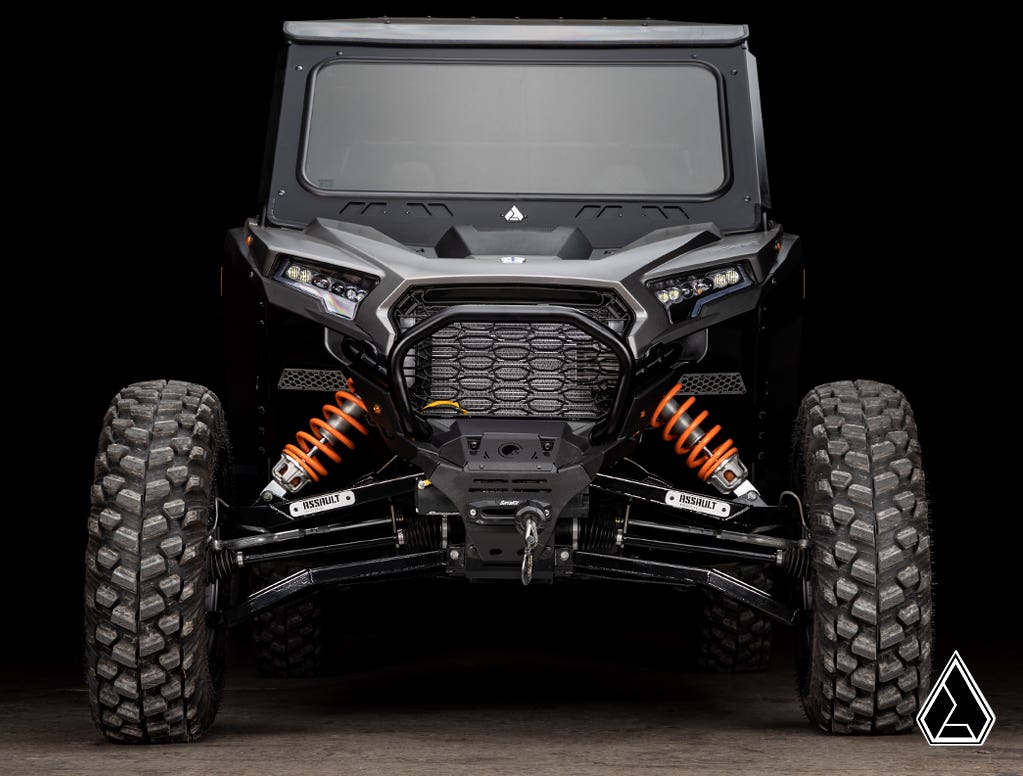 Front view of a black off-road vehicle with Assault Industries Polaris RZR XP High-Clearance 1.5 Forward Offset Boxed A-Arms, rugged tires, exposed orange suspension springs, angular body lines, bright headlights, winch, and hexagonal grille.