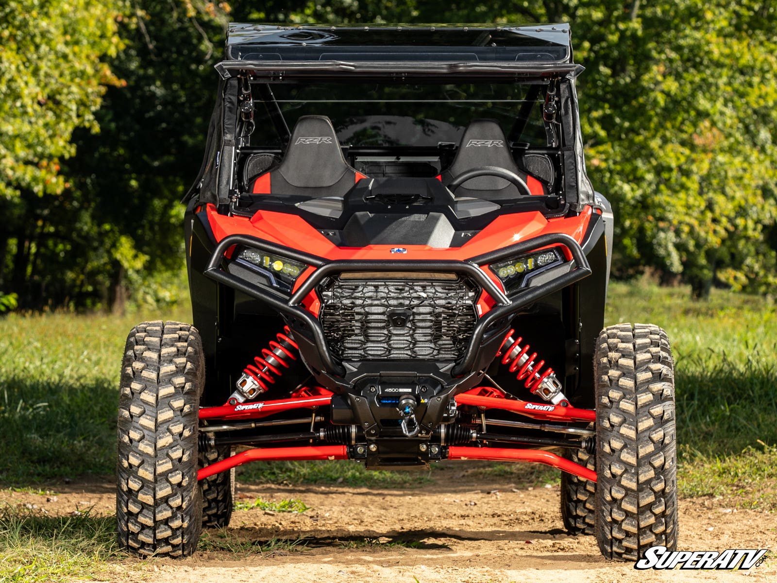 A Polaris RZR XP equipped with Inner Fender Guards sits on a dirt path surrounded by greenery, featuring large rugged tires, visible suspension, two seats, a black roof, and LED headlights. The SuperATV logo appears in the corner.